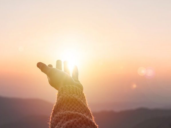 Young woman hand reaching for the mountains during sunset and beautiful landscape